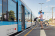 © 24K-Production - A person with a bicycle waits near an open train door at a busy railway station on a sunny day, ready to embark on their journey.