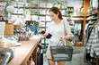 © zhouyilu - Young woman holding shopping basket while examining item in store