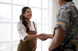 © Apichat - Smiling waitress shaking hands with customer in cafe
