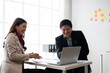 © Apichat - Business people laughing while working on laptop in office