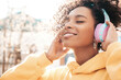 © halayalex - Beautiful black woman with afro curls hairstyle.Smiling model in yellow hoodie.Sexy carefree female enjoying listening music in wireless headphones.Posing on street background at sunset.Closed eyes