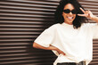 © halayalex - Beautiful woman with afro curls hairstyle.Smiling hipster model in white t-shirt. Sexy carefree female posing in the street near brown wall. Cheerful and happy, in sunglasses.Shows peace sign