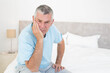 © WavebreakMediaMicro - Senior man sitting on bed edge in bright bedroom holding head in hand beside nightstand lamp