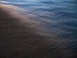 © Maciej Bonk - Gentle sea waves washing over the sand, creating a smooth abstract texture with soft light reflections