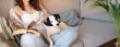 © Iryna&Maya - Reading with dog. White and black dog looking at camera while lying on laps of owner woman in blue jeans holding book. Weekend hobby time for relax and rest. long banner