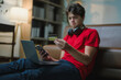 © PaeGAG - Teenager making an online payment while holding a credit card, using a laptop in the comfort of home during a cozy evening