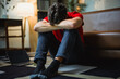 © PaeGAG - Depressed young male sitting on living room floor, head bowed between knees, expressing emotional distress and mental struggle