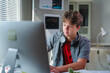 © PaeGAG - Teenage student wearing headphones, focusing intently on desktop computer during remote learning session at home workspace
