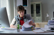 © PaeGAG - Professional worker handling paperwork at organized desk, wearing headphones near computer and document stacks, demonstrating workplace efficiency