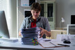 © PaeGAG - Young office worker looking at a large pile of paperwork on his desk, feeling overwhelmed and stressed