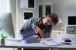 © PaeGAG - Young businessman yawning and making rock sign gesture while looking at pile of paperwork on desk in office