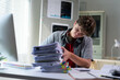 © PaeGAG - Overworked teenager struggling with a large stack of paperwork, showing frustration and stress in his home office