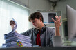© PaeGAG - Young businessman expressing frustration while managing a pile of documents at his desk in a busy office environment