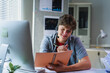 © PaeGAG - Happy young male call center operator wearing headset and taking notes while working on a computer