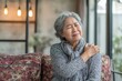 © LimeSky - Elderly Asian woman experiencing shoulder pain at home while sitting on the couch