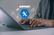 © MUNTHITA - Close-up of hands typing on laptop with virtual support icons, AI tools, chatbot and 24/7 service. Concept of customer support, digital technical assistance and remote help via modern technology.