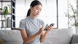 © Charlie's - Asian Woman controlling smart home. mobile phone with smart home app in living room. touch screen ai technology. Remote home control system