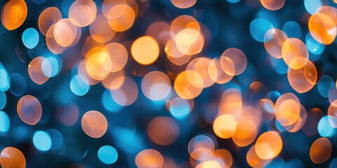 A blurred photograph captures a multitude of tiny lights, predominantly in shades of orange and blue, creating a bokeh effect against a dark background. 