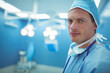 © wavebreak3 - Standing male surgeon under surgical lights in OR wearing scrubs stethoscope mask cap, copy space