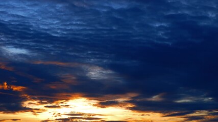 Wall Mural - A sunrise time-lapse reveals golden light breaking through dense, dark clouds, casting fiery tones across the sky, showcasing the powerful beauty and shifting patterns of nature’s weather at dawn.
