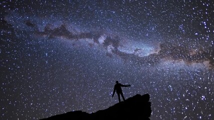 Wall Mural - silhouette of a person on a cliff under a starry sky, captured from a low angle. perfect for a video