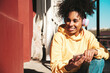 © halayalex - Beautiful woman with afro curls hairstyle.Smiling model in yellow hoodie.Sexy carefree female enjoying listening music in wireless headphones.Posing on street background at sunset