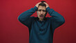 © Krakenimages.com - Young man in a blue hoodie shows emotional stress against a vivid red background, highlighting his expressive concern and latino features with impactful body language.