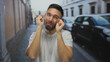 © Krakenimages.com - Young hispanic man in urban street setting making a mocking crying gesture, expressing sarcasm amid parked cars and buildings with an amused expression in daylight.