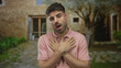 © Krakenimages.com - Man stands with crossed arms over chest at home entrance of stone building outdoors wearing pink shirt in daylight; gratitude.