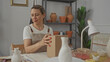 © Krakenimages.com - Woman opens cardboard box on studio table with pottery vases on shelves and art tools scattered; creativity fulfillment.