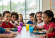 © StockHive - Diverse group of happy elementary school children eating lunch together at a table