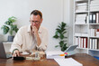 © Tj - Pensive mature accountant calculating budget and managing finances while sitting at desk, working with financial documents and utilizing a calculator in a modern office setting