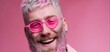 © Alba - The cheerful man with pink glasses and a vibrant expression against a pink background.