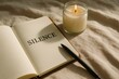 © Татьяна Евдокимова - Open notebook with silence written on it next to a burning candle and a pen on a beige bedsheet, perfect for a peaceful morning ritual