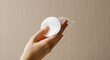 © hatkadigital - A hand holds two white round cotton pads The background is a beige textured surface
