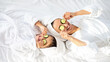 © Prostock-studio - Top view of playful mother and daughter in bathrobes and white towels on heads laying on bed, holding cucumber circles, making face care procedures at home. Motherhood, parenthood concept