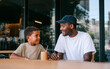 © Amy - Young father and little boy smiling and talking together while sitting at wooden table indoors