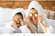 © Prostock-studio - Happy family young mother and daughter with cucumber circles on eyes and towels on head laying on bed, having spa day at home. Mom having beauty day with her little girl, bedroom interior