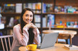 © Prostock-studio - Confident happy arab woman sitting at table in cafe with laptop computer and smiling to camera. Portrait of smiling lady freelancer posing in cafeteria while working remotely, free space