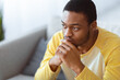 © Prostock-studio - Troubled black guy looking at copy space while thinking about something, sitting on couch in grey living room, closeup, panorama. Sad african american young man leaning on his hands, having problem
