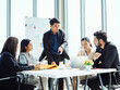 © AU USAnakul - Southeast Asian business professionals in formal attire gathered in modern office, leader presenting ideas while colleagues listen attentively, symbolizing teamwork, leadership, and corporate success.