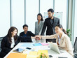 © AU USAnakul - Asian business team in modern office placing hands together on meeting table, smiling with confidence, symbolizing teamwork, unity, leadership, and motivation for corporate success.