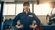 © Milan - Confident young Asian female mechanic in an auto repair shop. Empowered woman in overalls with hands on hips in a garage.