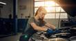 © Milan - Female mechanic working on a car engine in a sunlit garage. Young woman in overalls repairing a vehicle.