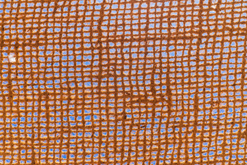Abstract texture background of a rustic brown jute hessian fabric, with a woven grid pattern against a bright blue sky.