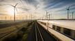 ©  S u n n y B u n n y - Modern high speed train on railway tracks passing through a scenic wind farm with rolling hills at golden hour.