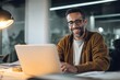 © SejutaCahaya - A smiling man working on a laptop in a modern office environment, with warm lighting and plants in the background, showcasing a productive and relaxed atmosphere