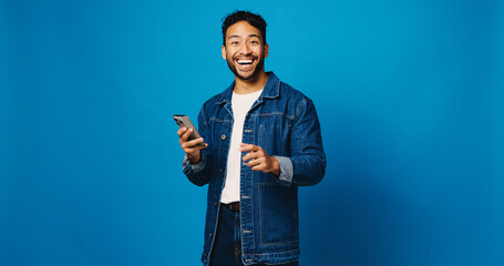 Surprise, phone and portrait with man in studio for social media giveaway, communication and success. Online prize, happiness with person on blue background for space, winner and competition