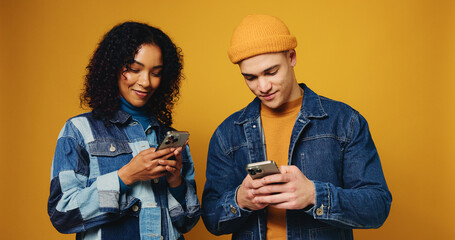 Phone, happy and couple in studio with networking, communication or chatting on mobile app. Smile, technology and man with woman on cellphone for contact on social media together by yellow background