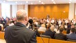 © Tan - Speaker addressing a large audience in a hall